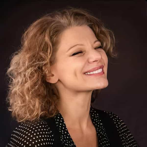 Portret al actriței Ofelia Popii, zâmbind, cu părul blond ondulat, pe un fundal întunecat.